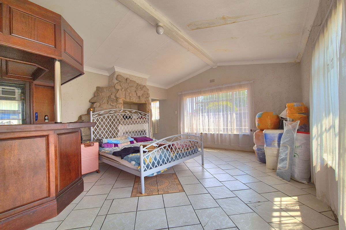 Spacious living area featuring a built-in bar, stone fireplace, and tiled flooring, offering potential for renovation and modernization.