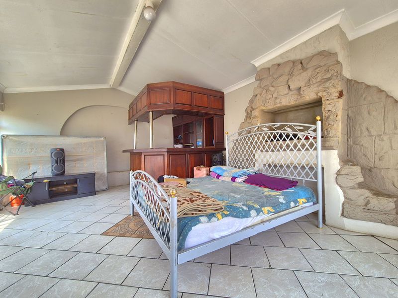 Covered patio area featuring a built-in wooden bar and a rustic stone fireplace, finished with tiled flooring.