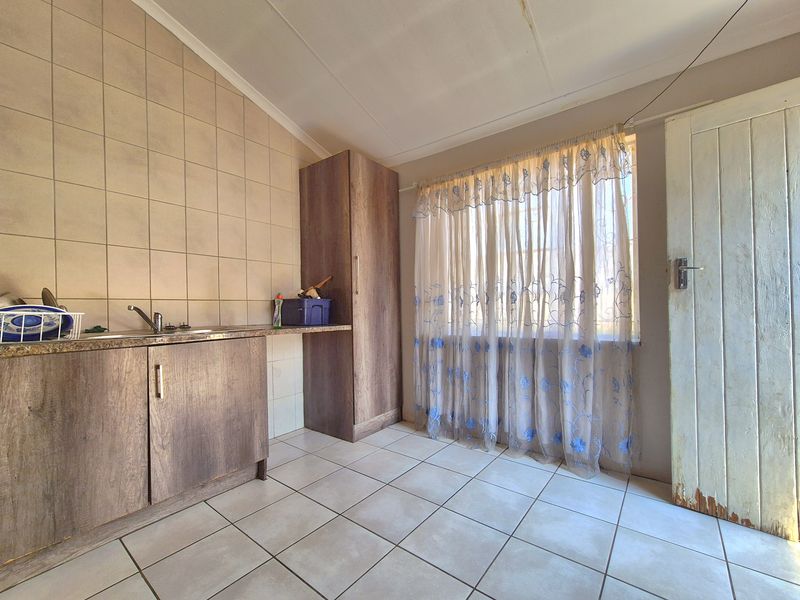 A functional kitchen area featuring built-in cabinetry, tiled backsplash, and tiled flooring, offering a clean and practical space for culinary activities.