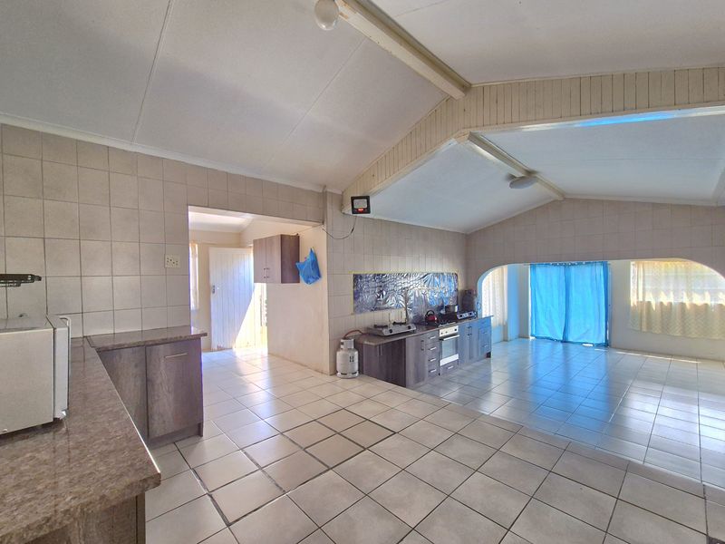 Spacious open-plan kitchen and living area featuring tiled flooring, vaulted ceilings, and built-in cabinetry, offering a blank canvas for renovation.