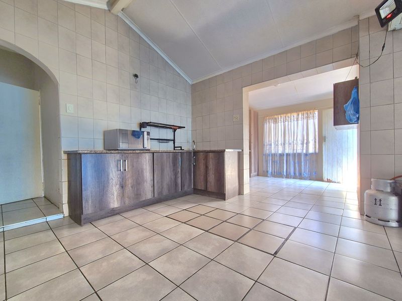 A functional kitchen area featuring tiled walls and flooring, laminate cabinetry, and a vaulted ceiling, offering a blank canvas for potential renovation.