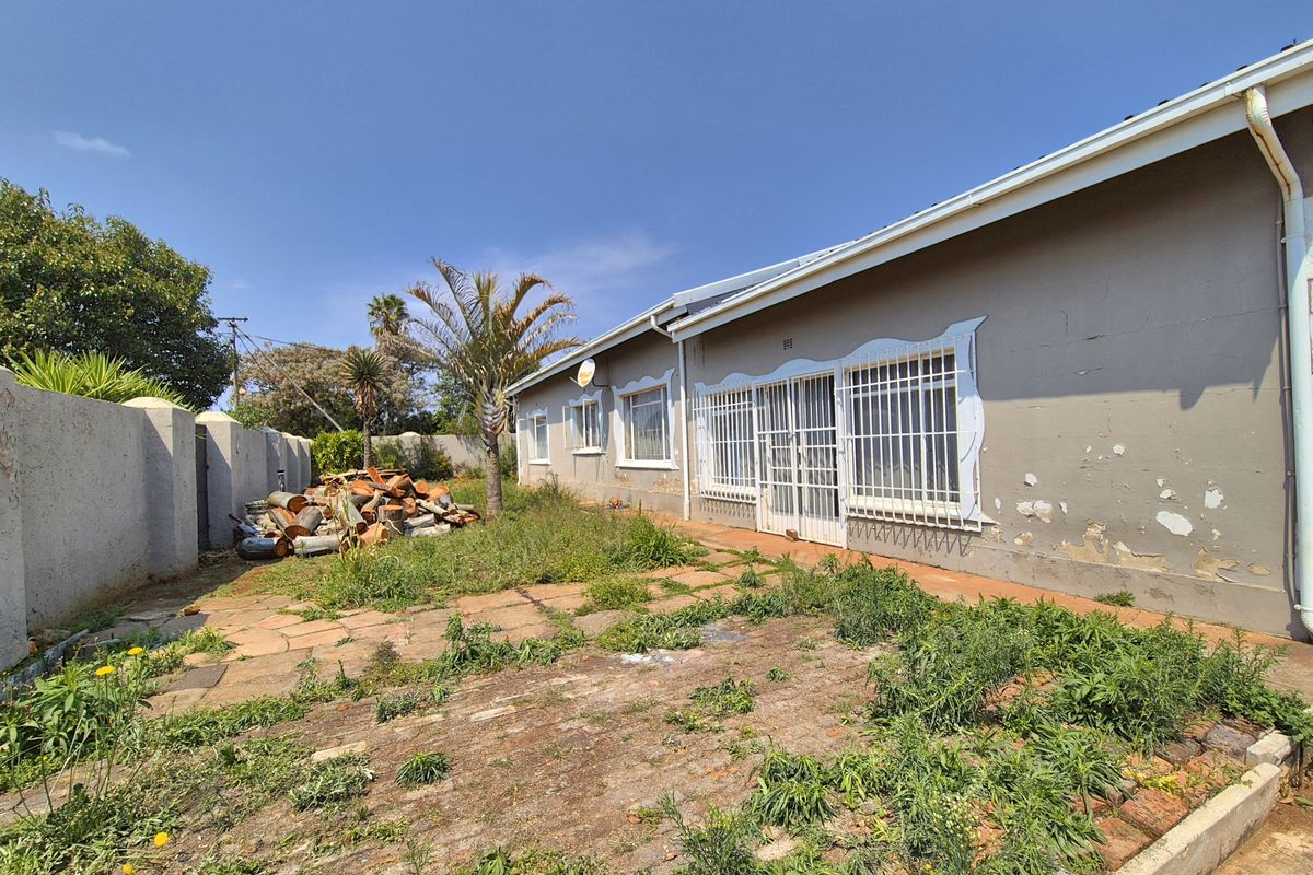 Rear exterior view of the property featuring a paved patio area, security bars on windows, and a boundary wall requiring maintenance and landscaping.