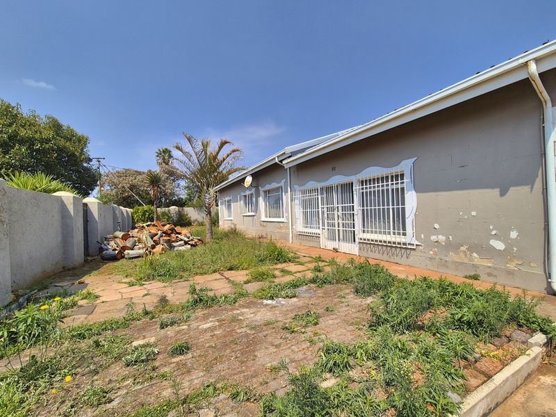 Rear exterior view of the property featuring a paved patio area, security bars on windows, and a boundary wall requiring maintenance and landscaping.