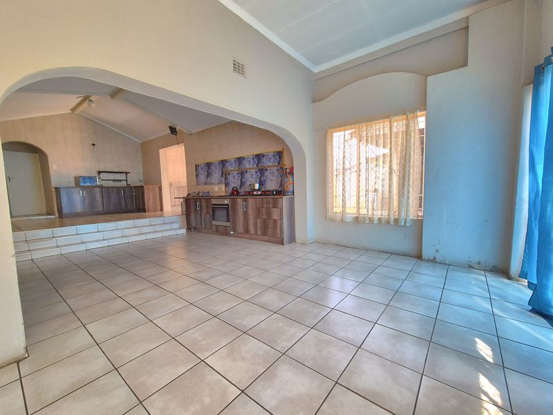 Spacious open-plan living and kitchen area featuring tiled flooring, built-in cabinetry, and a raised kitchen platform with an integrated oven and hob.