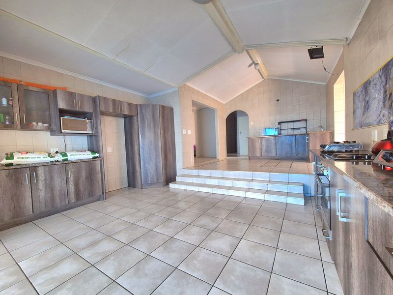Spacious kitchen featuring tiled flooring, built-in cabinetry, a gas hob, and a raised platform area with an archway leading to adjacent rooms.