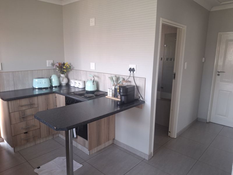 Compact kitchen featuring wood-look cabinetry, dark laminate countertops, built-in electric hob and oven, with tiled flooring and direct access to an adjacent room.