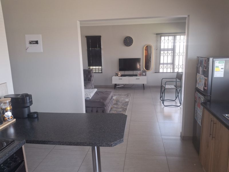 Open-plan living area featuring tiled floors, a kitchen breakfast bar, and natural light through windows fitted with security bars and blinds.