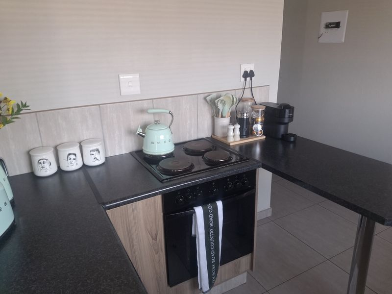 A compact kitchen area featuring a built-in oven, electric hob, modern laminate cabinetry, and a breakfast bar extension with tiled flooring.