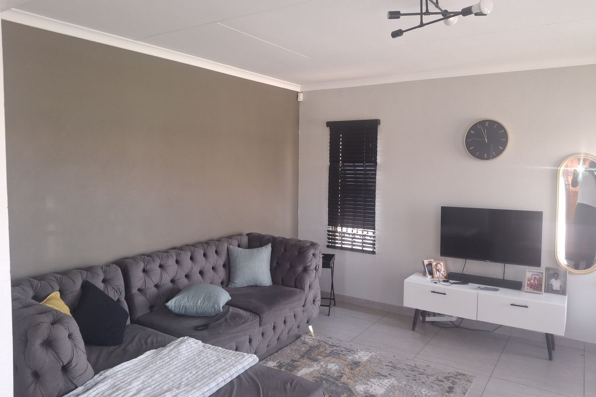 A well-maintained living room featuring neutral wall tones, tiled flooring, and modern venetian blinds, providing a comfortable and functional living space.
