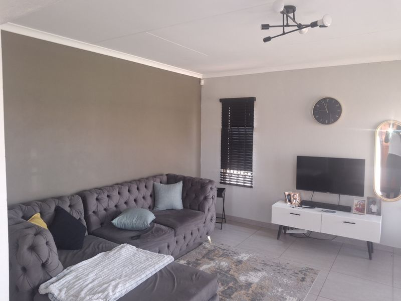 A well-maintained living room featuring neutral wall tones, tiled flooring, and modern venetian blinds, providing a comfortable and functional living space.