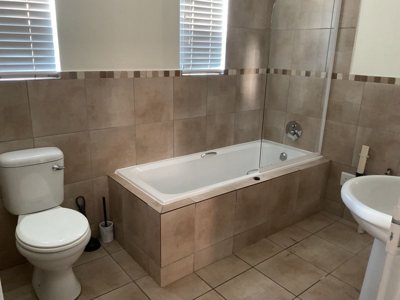 A functional bathroom featuring a built-in bathtub with a glass shower screen, pedestal basin, toilet, and neutral tiled finishes throughout.