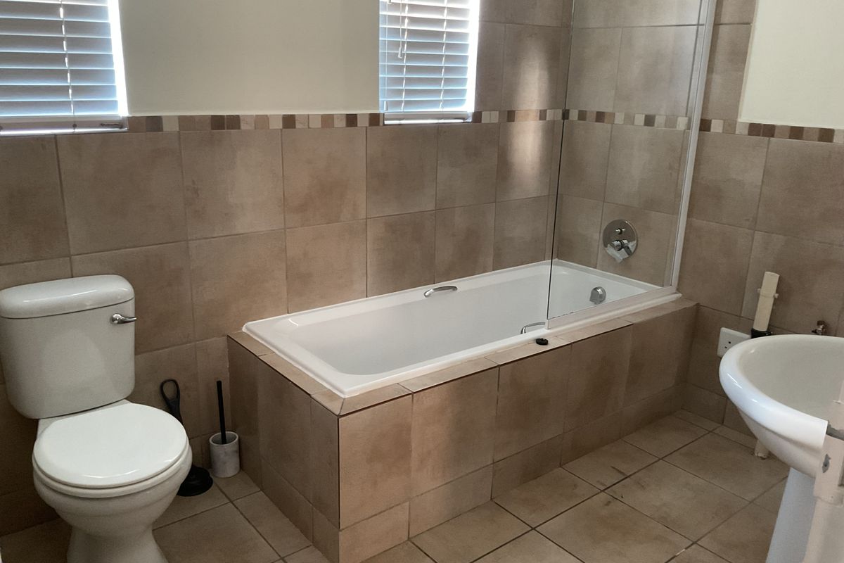 A functional bathroom featuring a built-in bathtub with a glass shower screen, pedestal basin, toilet, and neutral tiled finishes throughout.