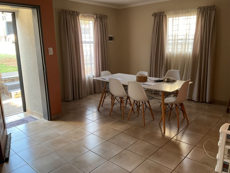 A functional dining room featuring tiled flooring, natural light through dual windows with security bars, and direct access to the exterior.