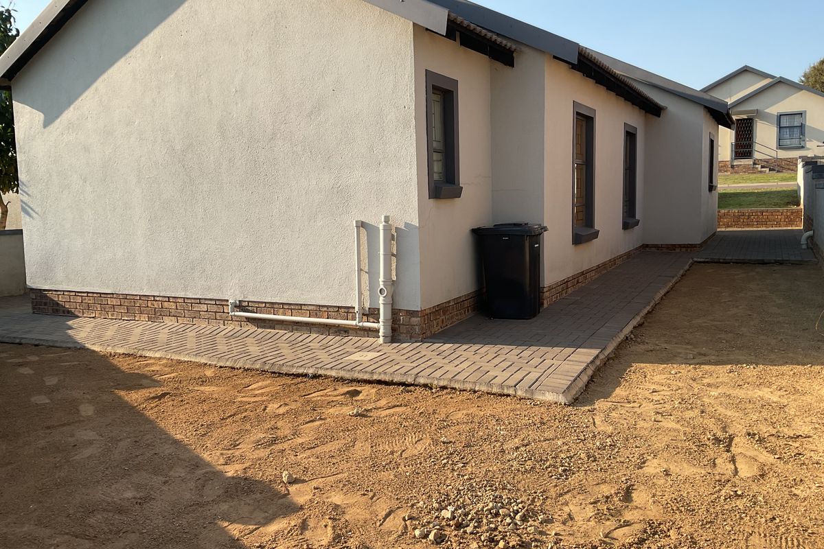 Rear exterior view of the house featuring paved walkways, brick plinth detailing, and unfinished garden area.