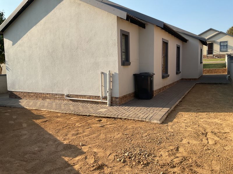 Rear exterior view of the house featuring paved walkways, brick plinth detailing, and unfinished garden area.