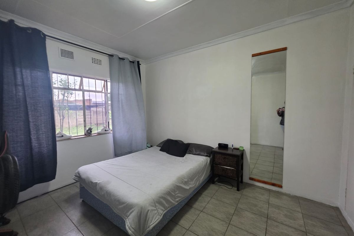 A functional bedroom featuring tiled flooring, a large built-in wall mirror, and a steel-framed window providing natural light.