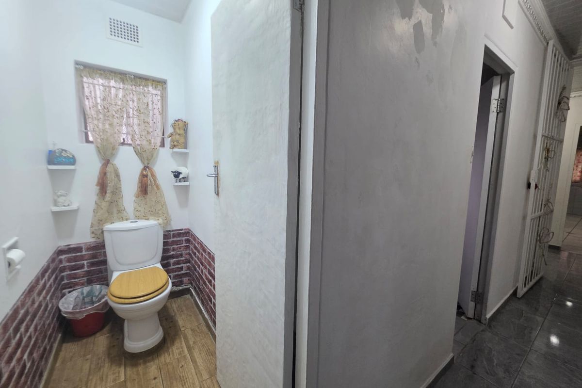 A small bathroom featuring a toilet, wood-look tiled flooring, and brick-effect wall accents, requiring some cosmetic attention to the wall finishes.