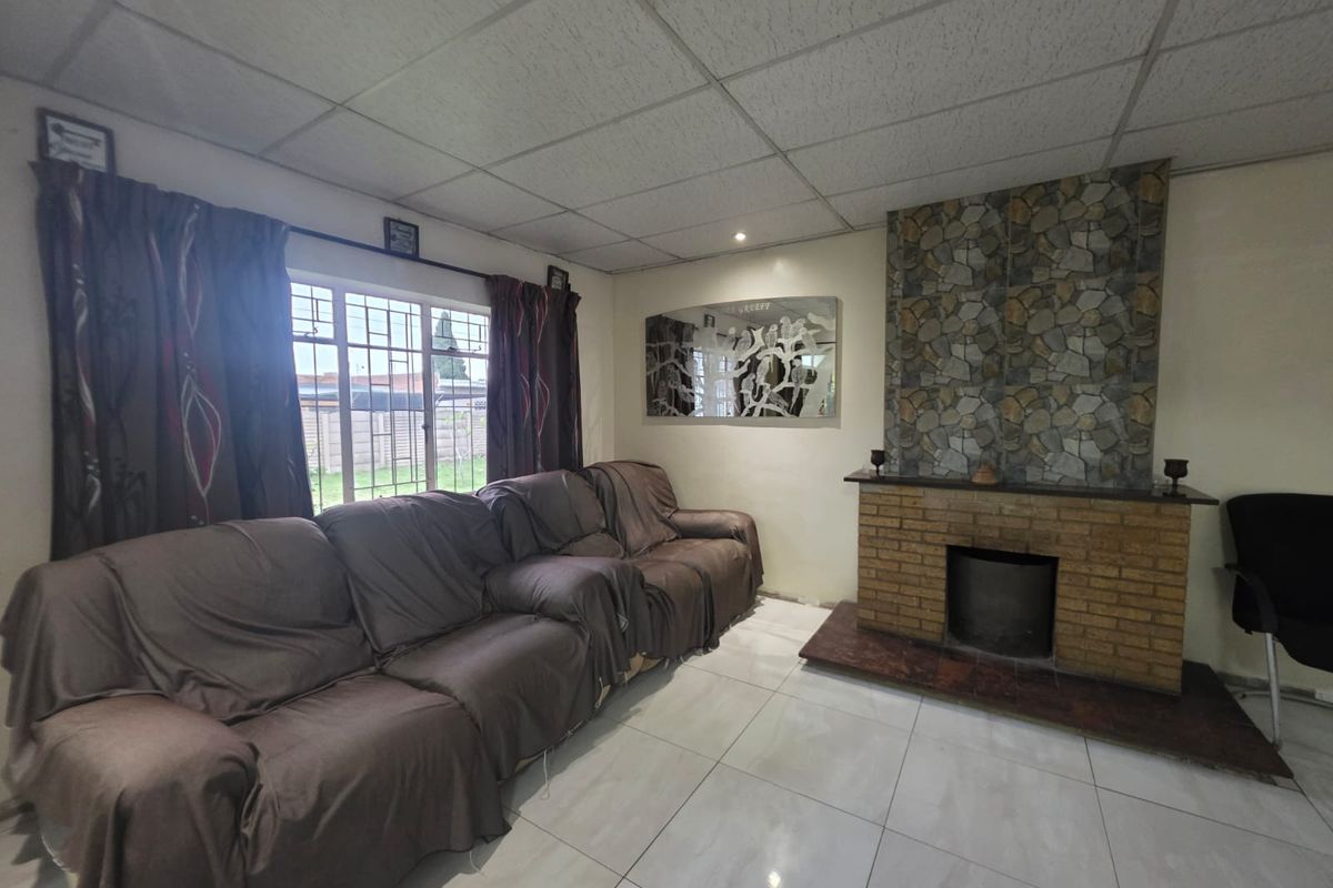 Living room featuring a brick fireplace with a stone feature wall, tiled flooring, and a drop ceiling.
