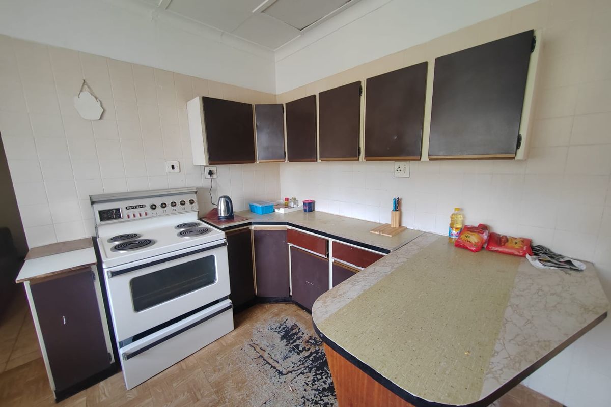 A functional kitchen featuring dated cabinetry, laminate countertops, and a freestanding electric stove with tiled splashbacks, offering potential for a modern renovation.
