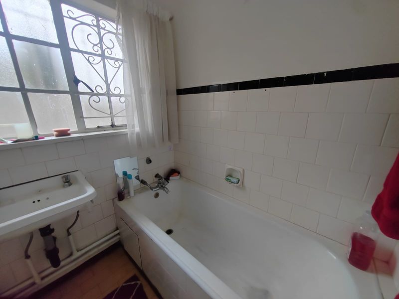 A dated bathroom featuring a built-in bathtub, wall-mounted basin, and classic tiled splashbacks, offering significant potential for a modern renovation.