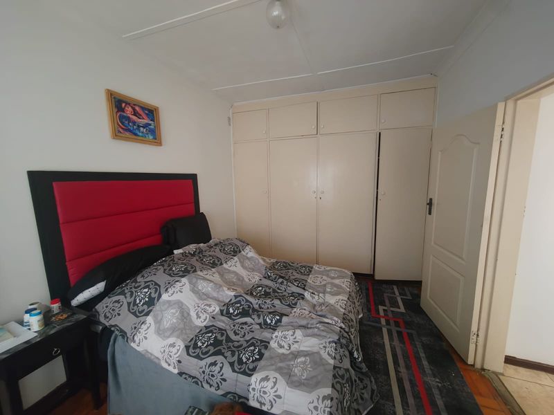 A bedroom featuring built-in cupboards, timber flooring, and a panelled door, offering a functional space with potential for cosmetic updates.