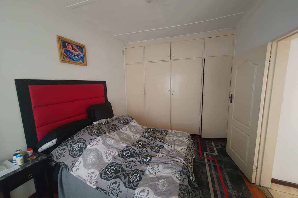 A bedroom featuring built-in cupboards, timber flooring, and a panelled door, offering a functional space with potential for cosmetic updates.