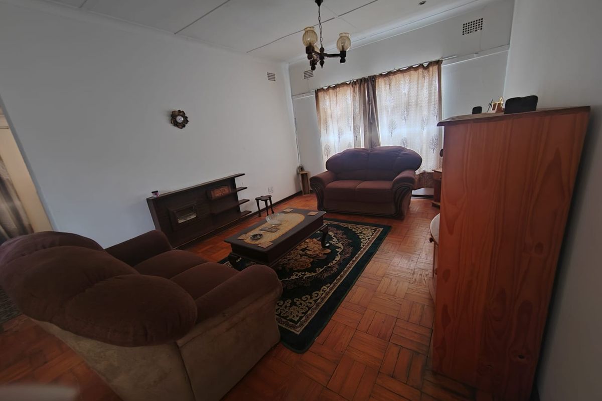 A living room featuring traditional parquet flooring, a central chandelier, and classic ceiling tiles, offering a dated but functional space ready for modernization.