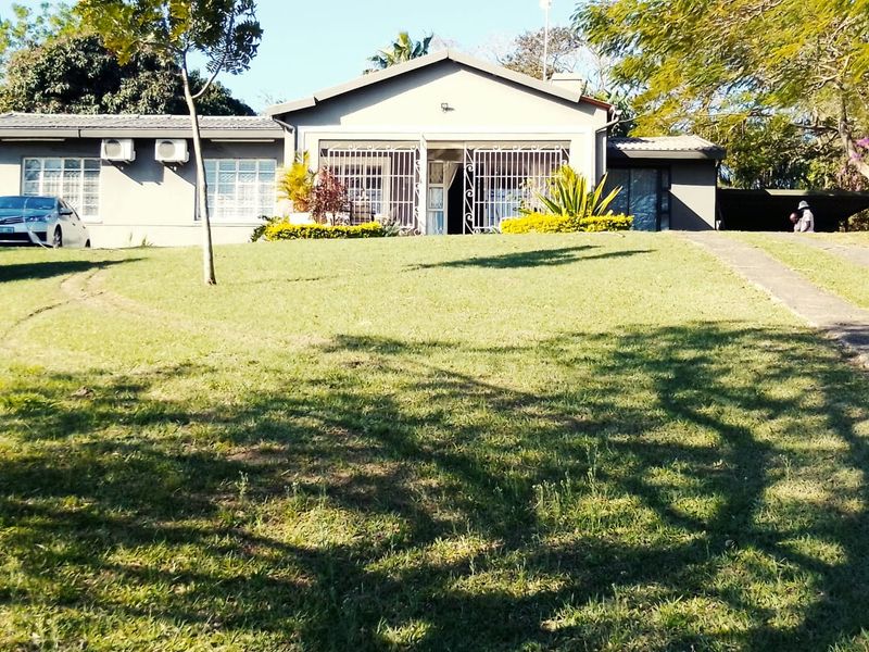 Front view of a single-story residential house featuring a large lawn, paved driveway, and security gates on the main entrance.
