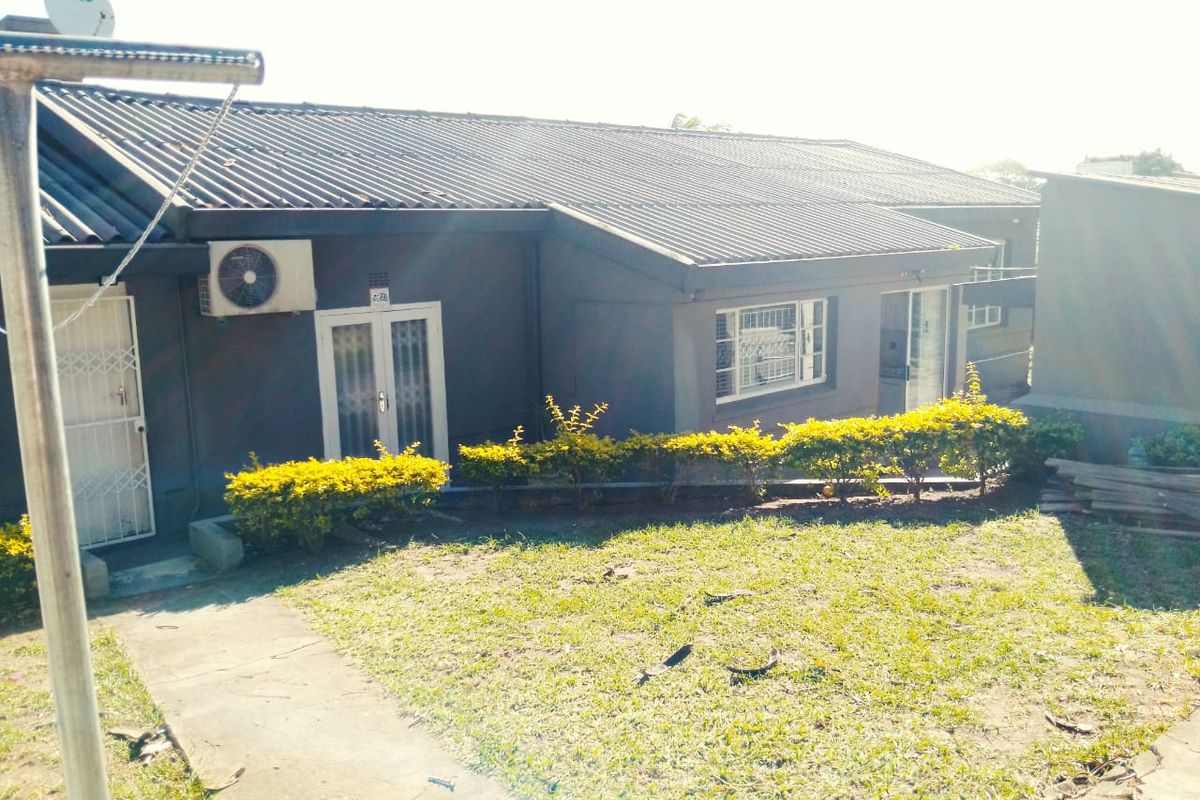 Rear view of the house featuring a corrugated metal roof, exterior air conditioning unit, security gates, and a paved walkway leading to the garden.