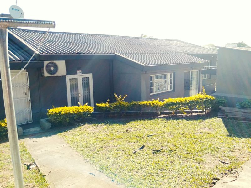 Rear view of the house featuring a corrugated metal roof, exterior air conditioning unit, security gates, and a paved walkway leading to the garden.