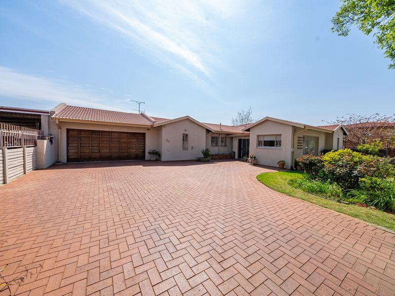 Front elevation of a single-story house featuring a large paved driveway, double garage, and well-maintained garden area.