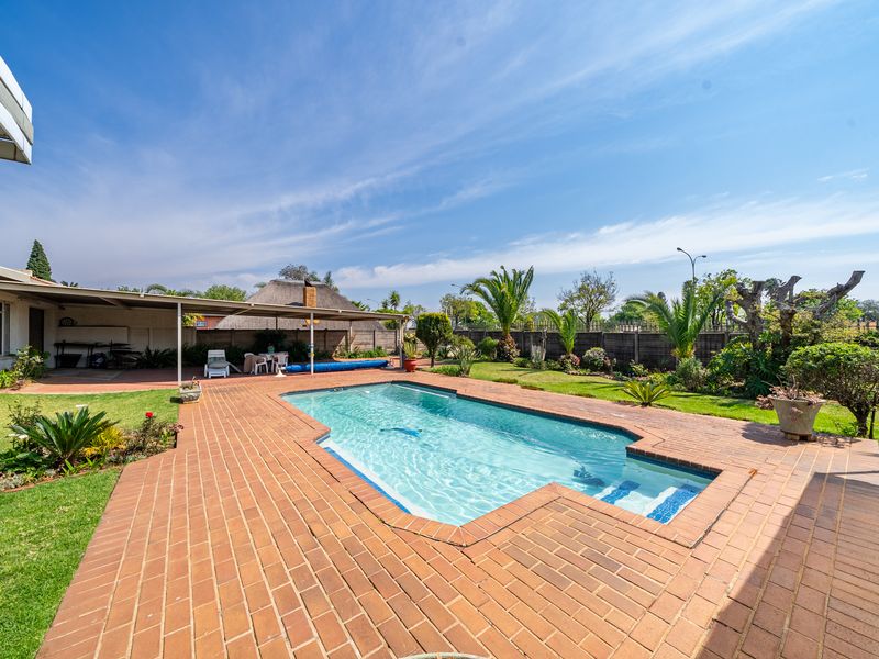 Spacious backyard featuring a swimming pool, brick-paved surround, covered patio area, and a separate thatched lapa in a well-maintained garden setting.