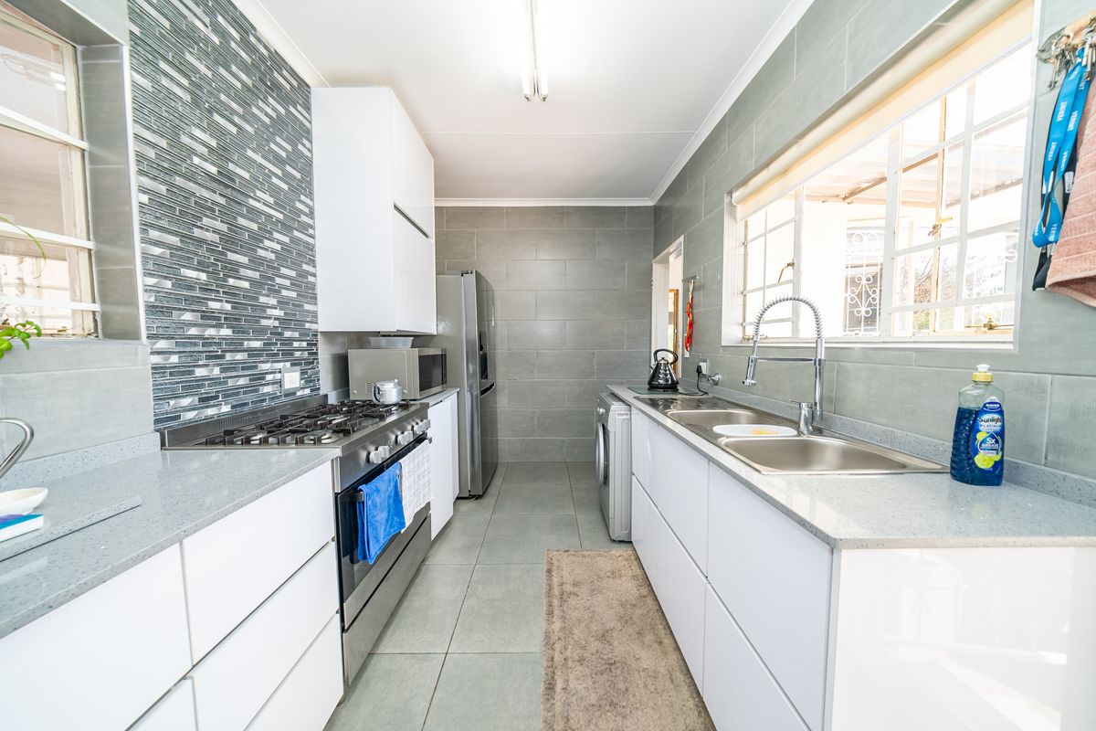 Modern galley-style kitchen featuring white cabinetry, stone countertops, a gas stove, and a double basin sink with tiled finishes throughout.