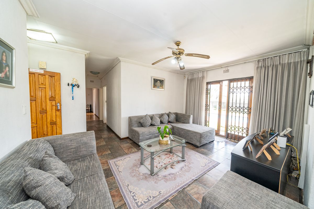 A spacious living room featuring tiled flooring, a ceiling fan, and sliding glass doors with security gates leading to the exterior.