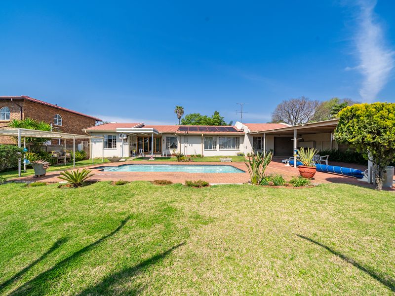 Rear view of the property featuring a swimming pool, paved patio area, covered carport, and a well-maintained garden with solar panels on the roof.
