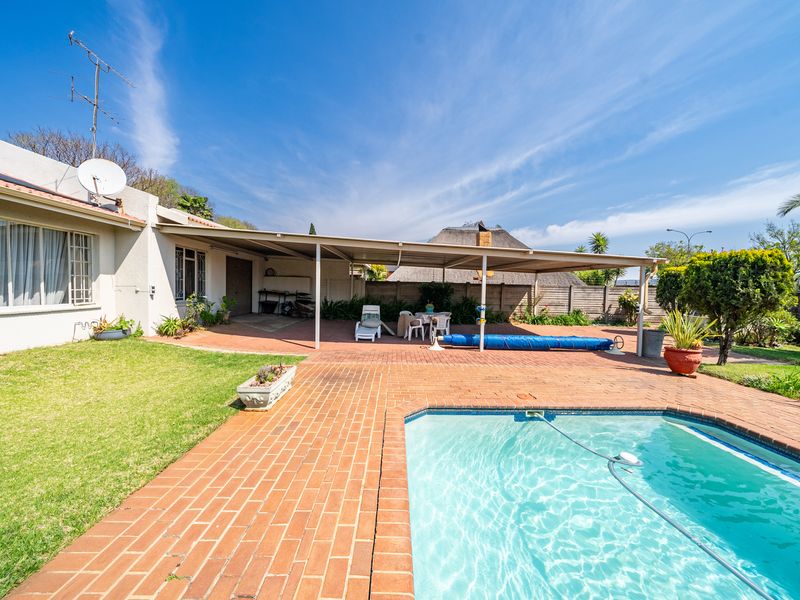 Rear exterior view featuring a swimming pool, paved patio area, and covered outdoor entertainment space set within a private garden.