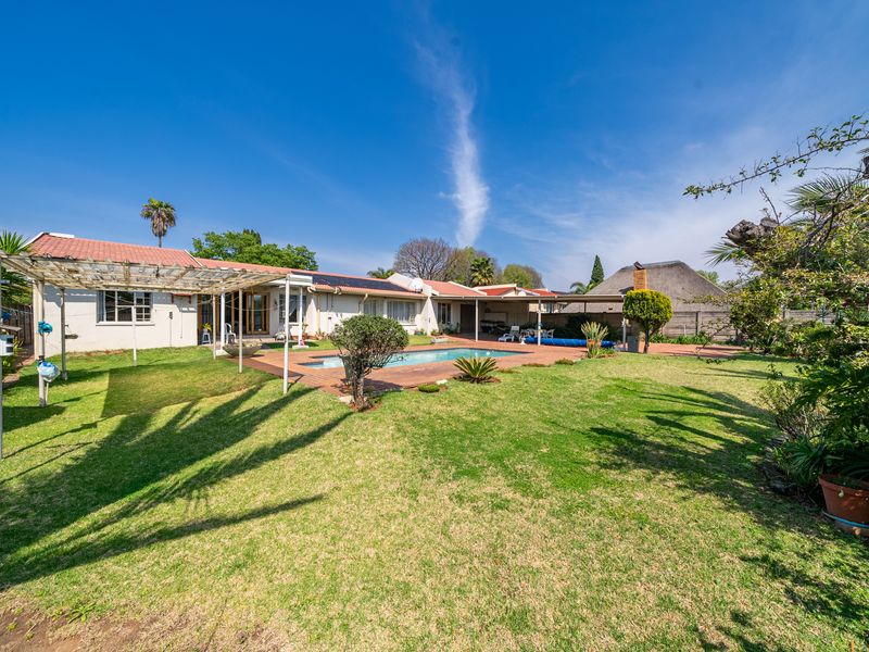 Spacious rear garden featuring a swimming pool, paved patio area, and a pergola, set against the rear elevation of the house with solar panels.