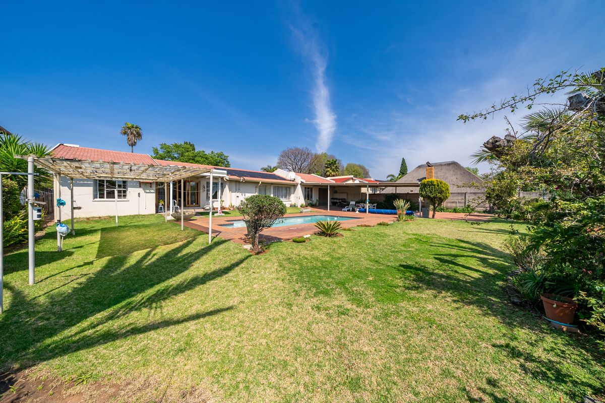 Spacious rear garden featuring a swimming pool, paved patio area, and a pergola, set against the rear elevation of the house with solar panels.