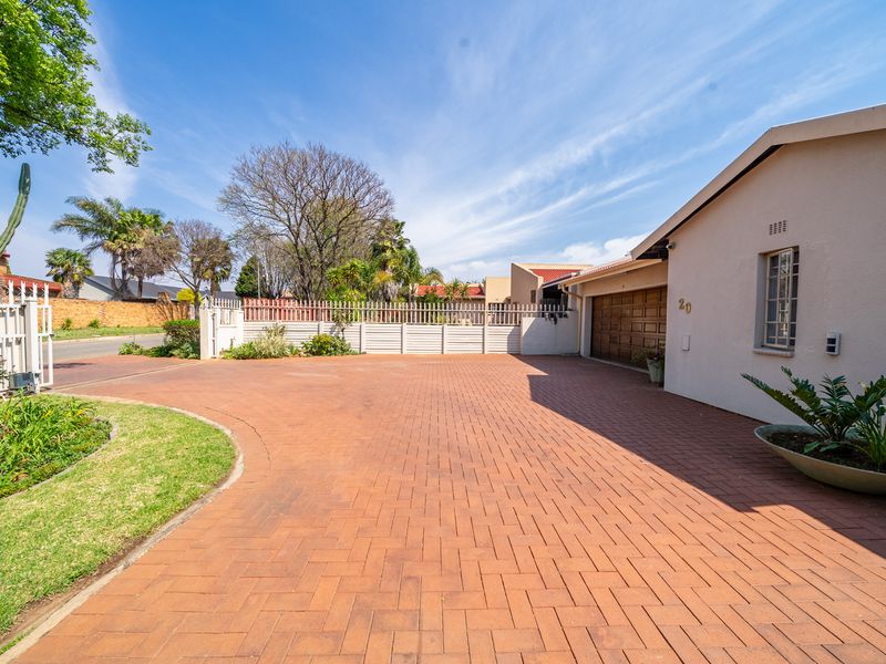 Front exterior view of the property featuring a spacious paved driveway, secure perimeter fencing, and a garage entrance.