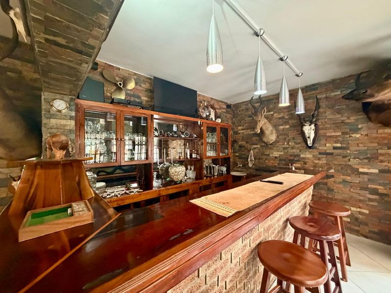 A rustic-style home bar featuring a built-in wooden counter, brick wall cladding, integrated cabinetry, and pendant lighting.