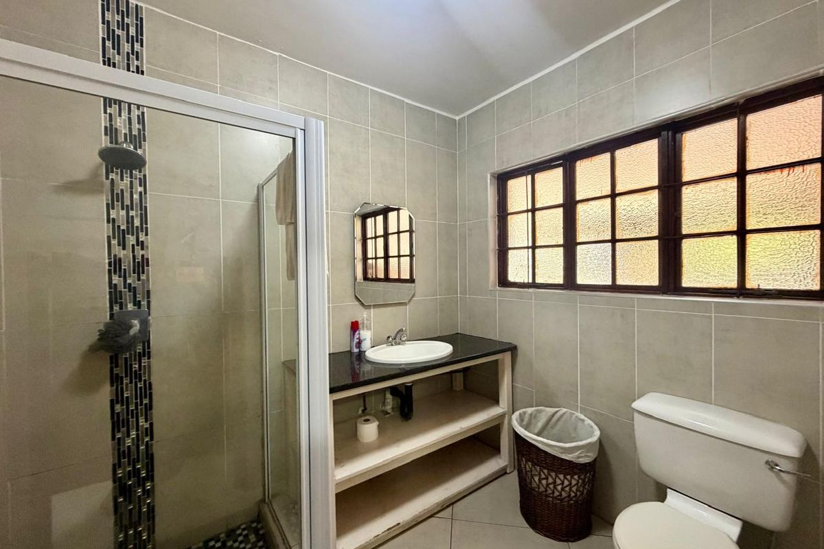 A functional bathroom featuring a shower enclosure, a vanity with a stone countertop, and a drop-in basin, finished with neutral wall and floor tiles.