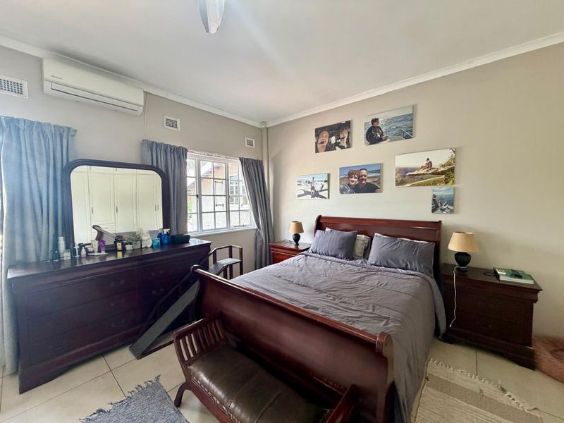 A well-lit bedroom featuring tiled flooring, built-in cupboards, and a wall-mounted split-system air conditioner.