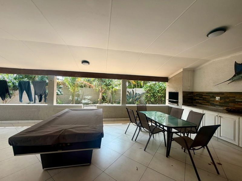 Spacious covered patio featuring a built-in braai, tiled flooring, and integrated cabinetry, offering a functional outdoor entertainment area overlooking the garden.