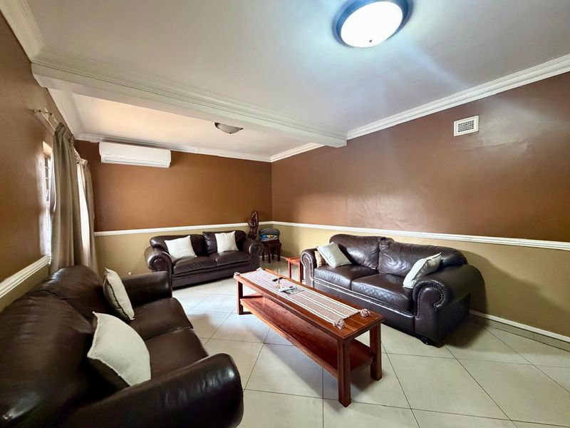 A spacious living room featuring ceramic tile flooring, crown molding, chair rail detailing, and a wall-mounted split-system air conditioner.