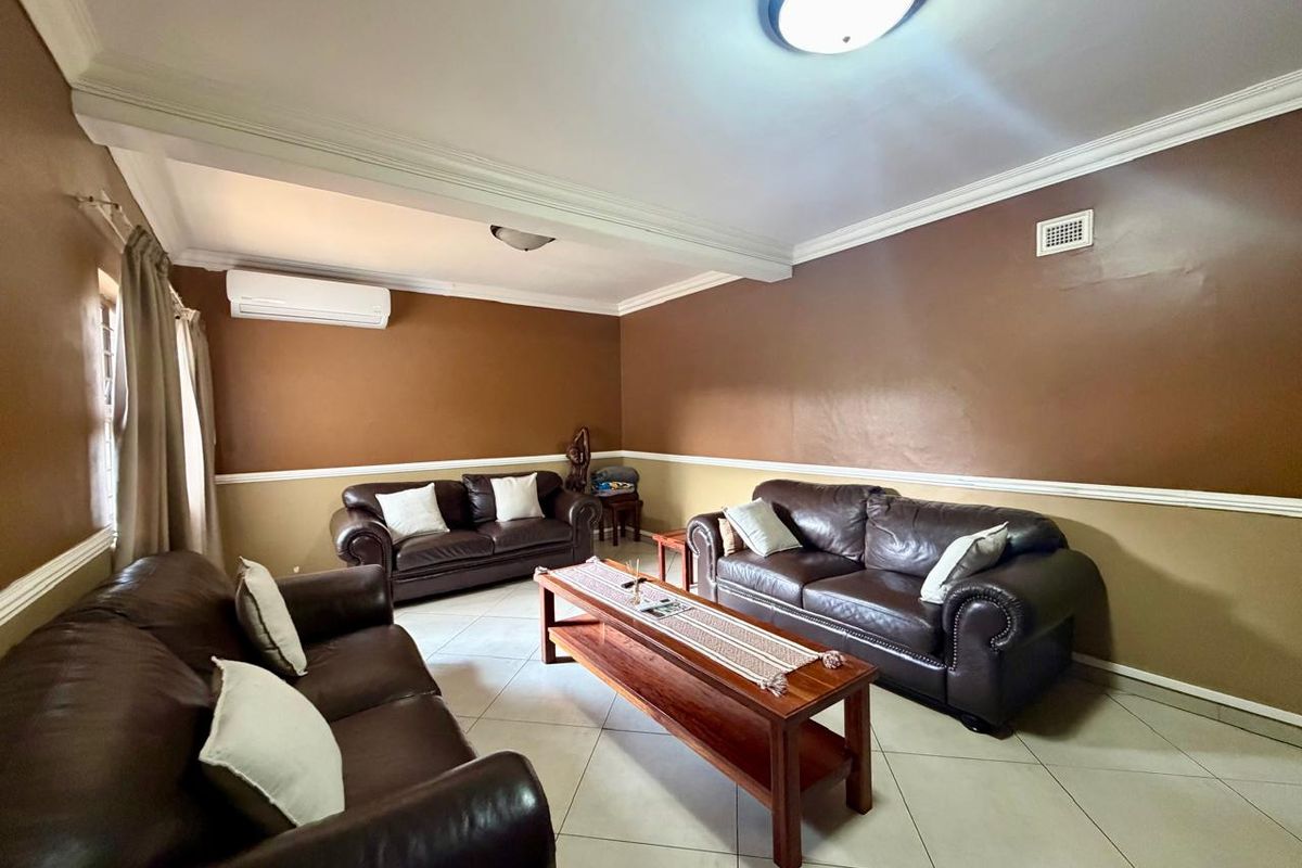 A spacious living room featuring ceramic tile flooring, crown molding, chair rail detailing, and a wall-mounted split-system air conditioner.