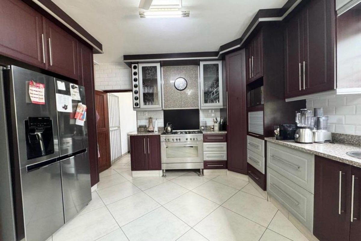 A well-maintained kitchen featuring dark wood cabinetry, granite countertops, a gas stove with extractor, and light-colored tiled flooring.