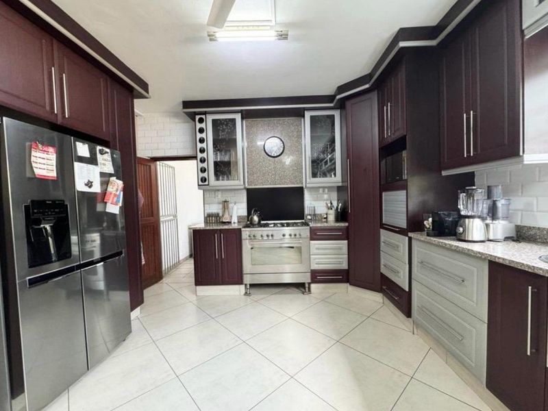 A well-maintained kitchen featuring dark wood cabinetry, granite countertops, a gas stove with extractor, and light-colored tiled flooring.