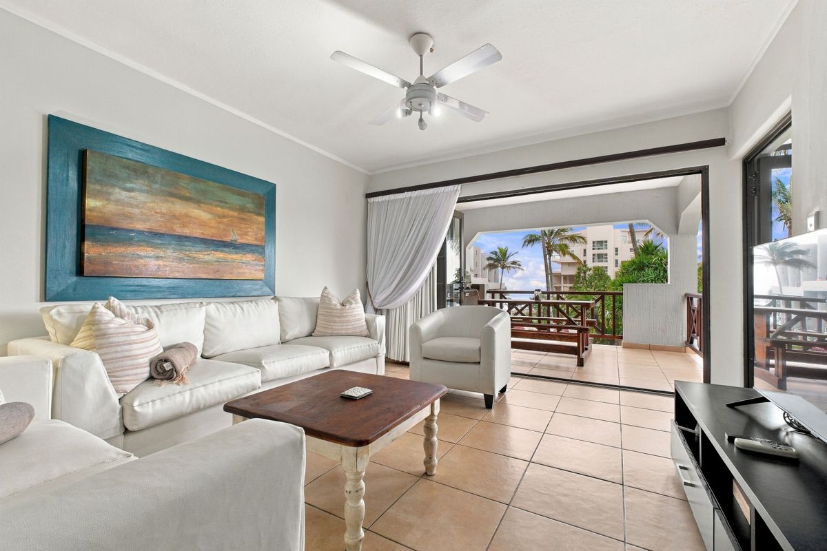 Bright living room featuring tiled flooring, a ceiling fan, and large sliding glass doors that open onto a covered balcony with outdoor views.