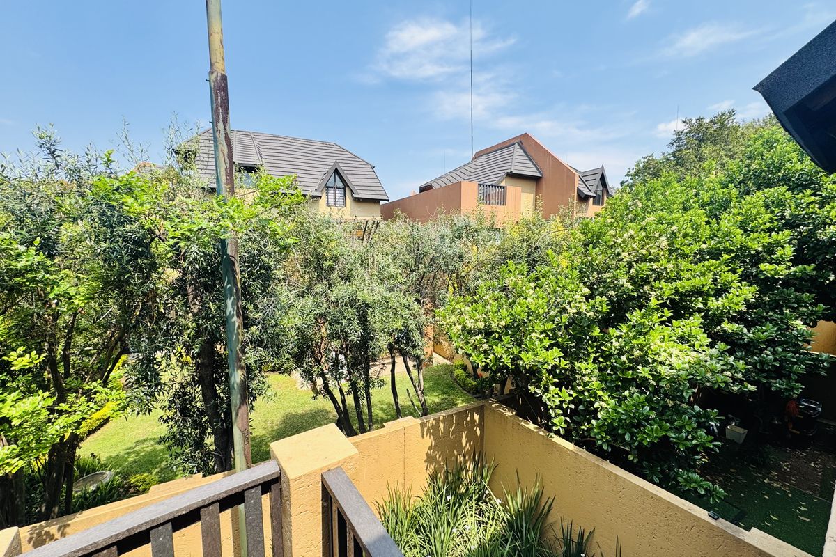 View from a balcony overlooking a private garden area with mature trees and neighbouring residential properties.
