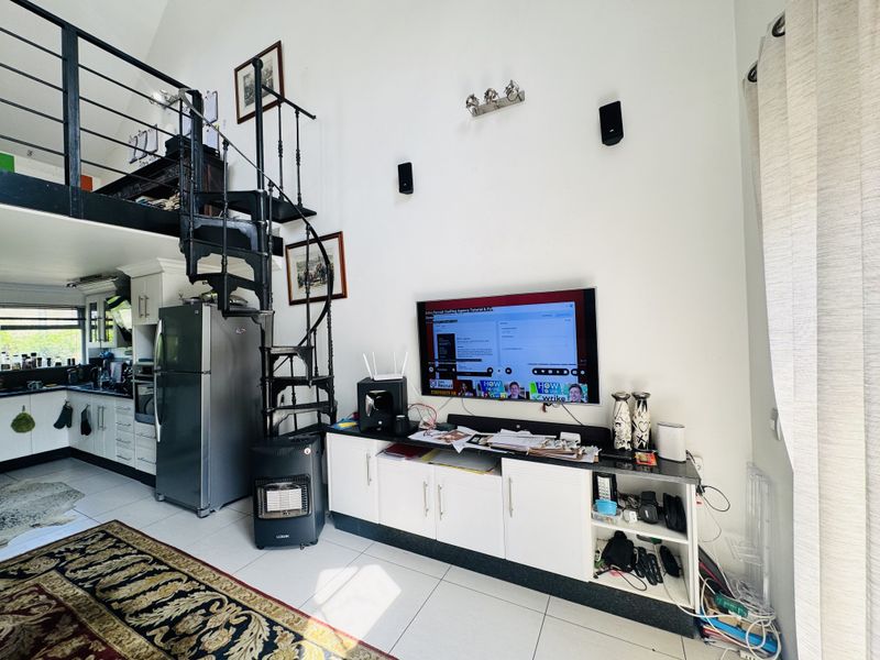 Open-plan living area featuring a spiral staircase leading to a mezzanine level, tiled floors, and integrated kitchen cabinetry.